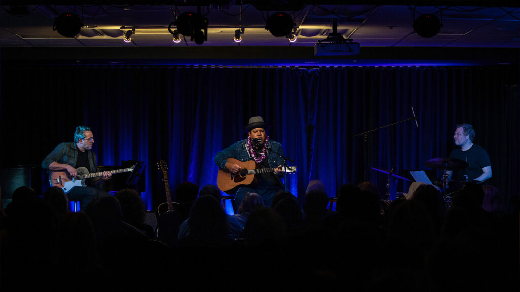 Chris Pierce performing on stage under blue lights during a concert at the Museum of Making Music.