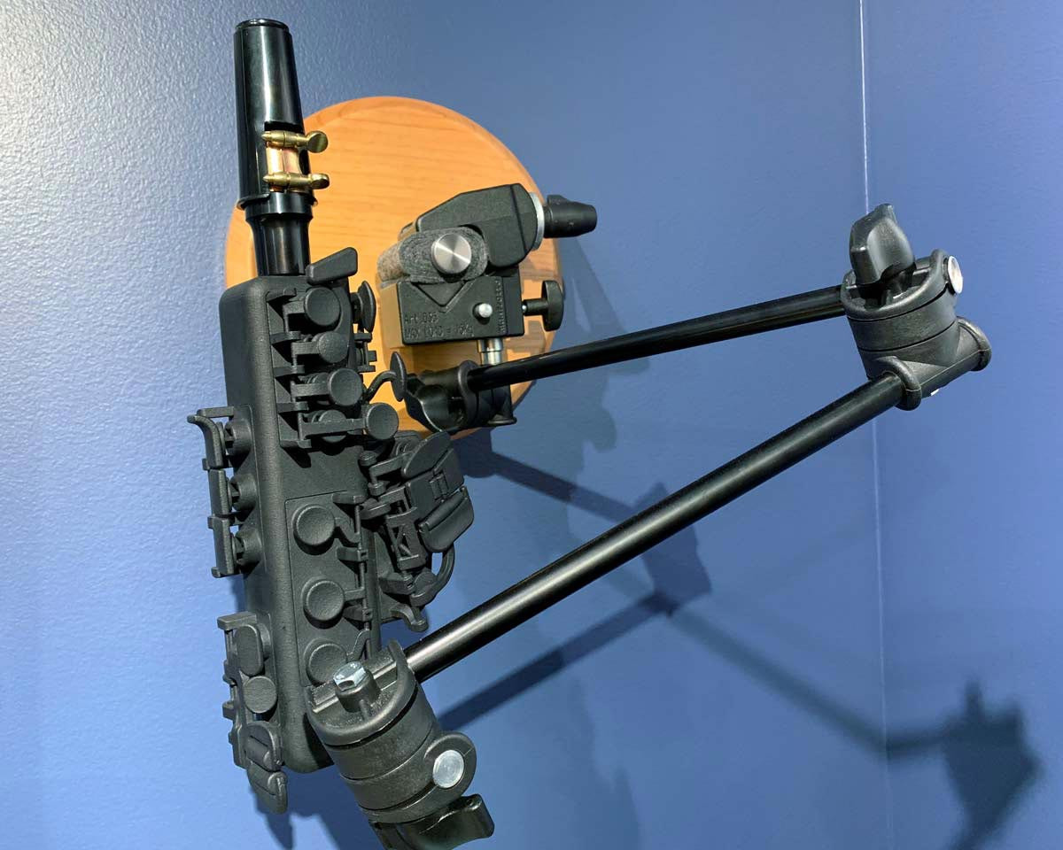 Black Odisei Music Travel Sax mounted on an articulating arm attached to a blue gallery wall