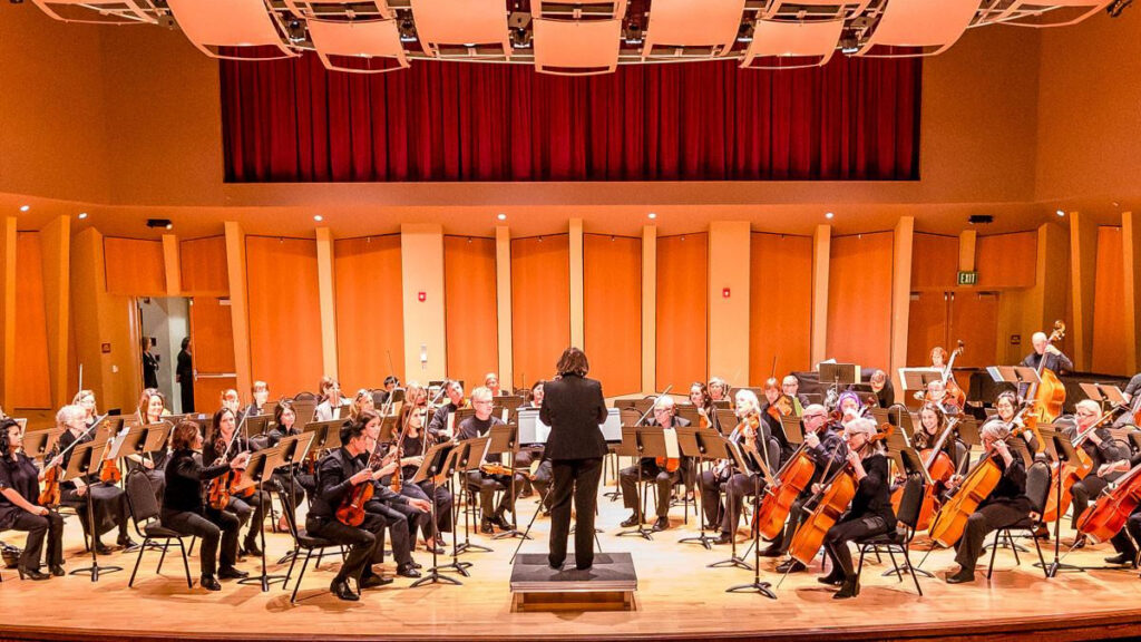 A conductor leading the North Coast Strings Orchestra on a concert hall stage