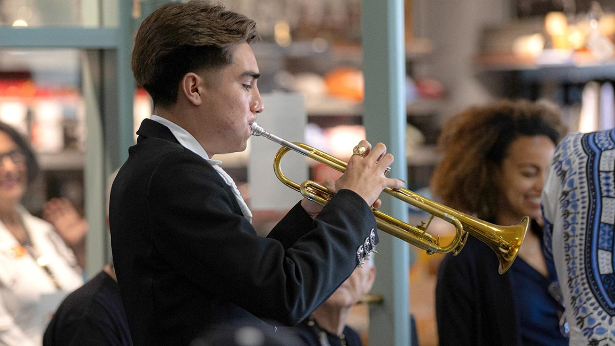 A young trumpet player in a black jacket performs among a crowd of museum visitors