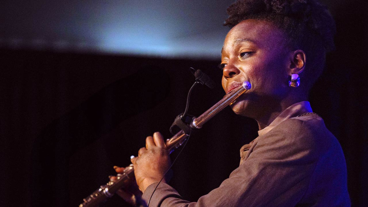 A flutist plays with eyes closed under blue and purple stage lighting