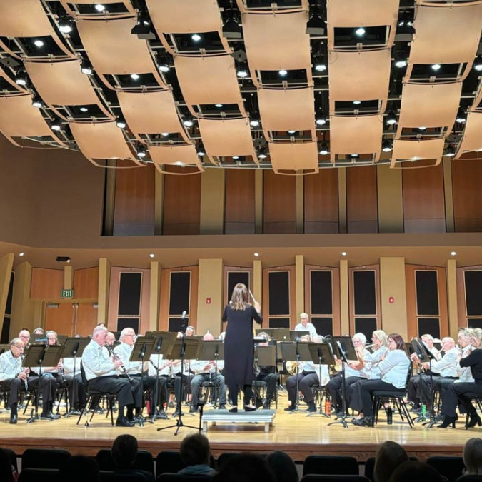 A conductor leading the New Horizons Band on a concert hall stage