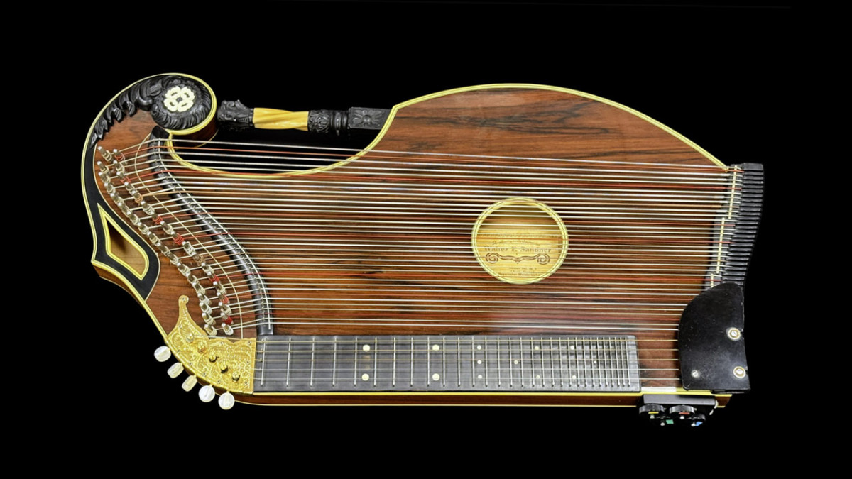 Walter E. Sandner concert zither with a dark wood-grain body, gold trim, carved scroll headstock, and fretted fingerboard on a black background