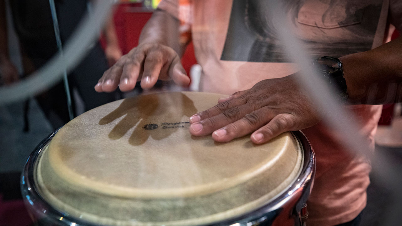 A visitor plays a conga drum with both hands during a hands-on program at the Museum of Making Music