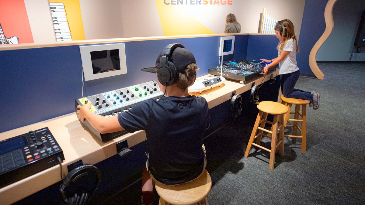 Two young visitors using electronic music production stations in the museum's interactive area